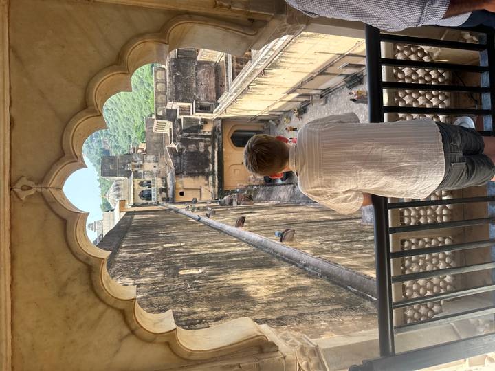 A boy gazes over the massive sandstone walls and courtyards of Amber Fort with green hills beyond.