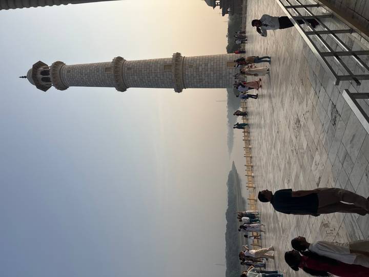 Marble minaret of the Taj Mahal complex overlooking the Yamuna River with visitors on the terrace.