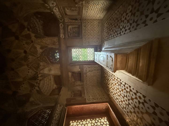 Dimly lit interior chamber with an ornate stone cenotaph and patterned marble floor inside the Taj Mahal complex.