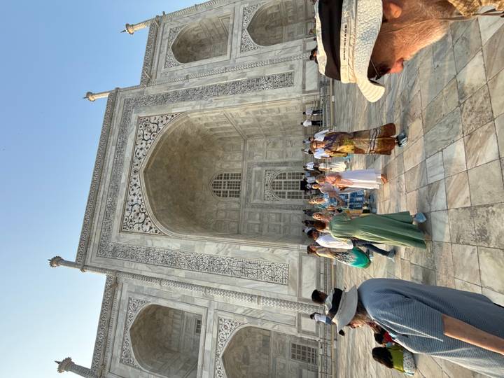 Tourists gather at the towering marble entrance of the Taj Mahal under a clear blue sky.