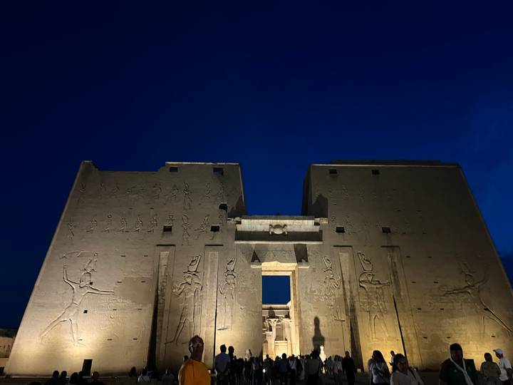 Edfu Temple façade lit against a deep blue evening sky displaying carved reliefs.