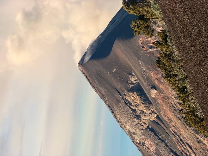 A dramatic volcanic cone emits a plume of smoke under soft evening light.