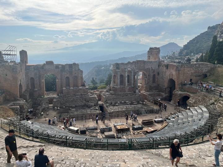 Ruins of the ancient Greco-Roman theatre in Taormina with distant Mount Etna and valley views.