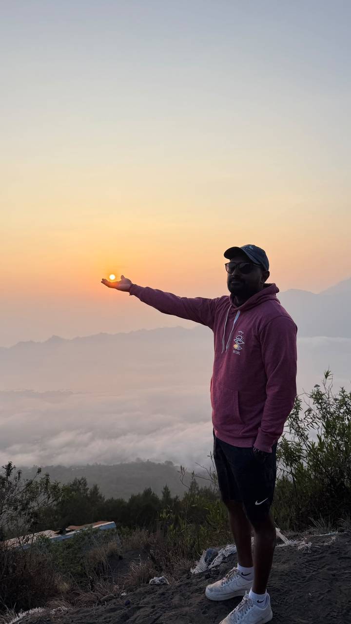A traveler playfully holds the rising sun in his palm atop a misty mountain viewpoint.