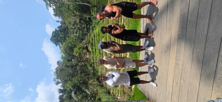 Five friends strike playful poses on a wooden deck overlooking lush rice terraces.