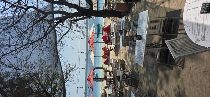 Beachfront café with red umbrellas and wooden tables overlooking turquoise water.