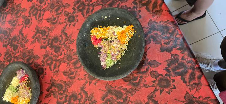 Crushed flower petals arranged in a heart shape on a black stone plate atop a red patterned tablecloth.