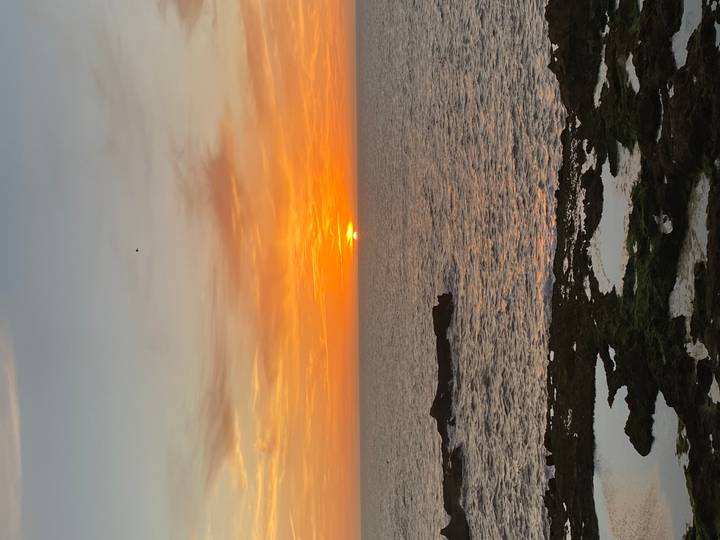 Brilliant orange sun sets over the Atlantic, tinting the sky and tide pools along a rocky shoreline.