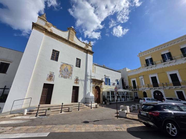 Whitewashed church and surrounding colourful buildings under a bright blue sky.