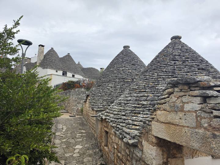 Close-up of the grey stone cone roofs of several trulli against an overcast sky.