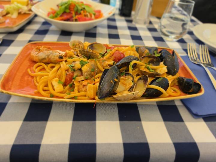 Plate of seafood pasta with mussels and clams on a blue-checked tablecloth.