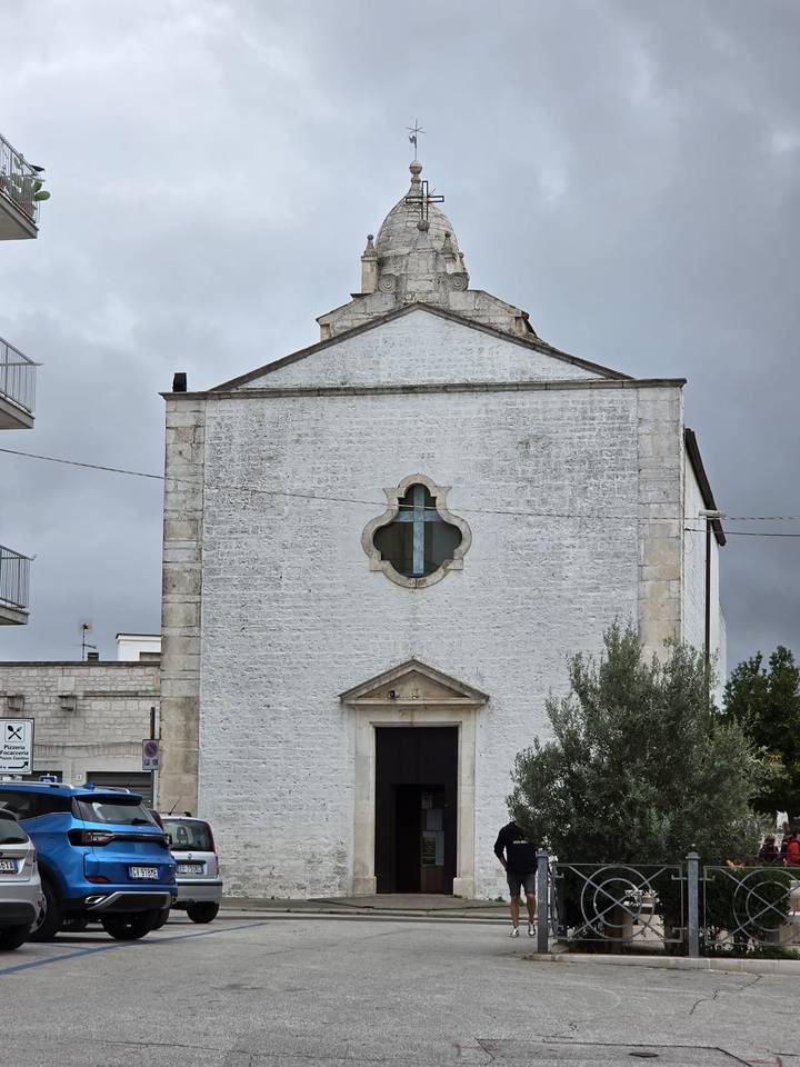 Simple white stone church façade with small quatrefoil window on a grey day.