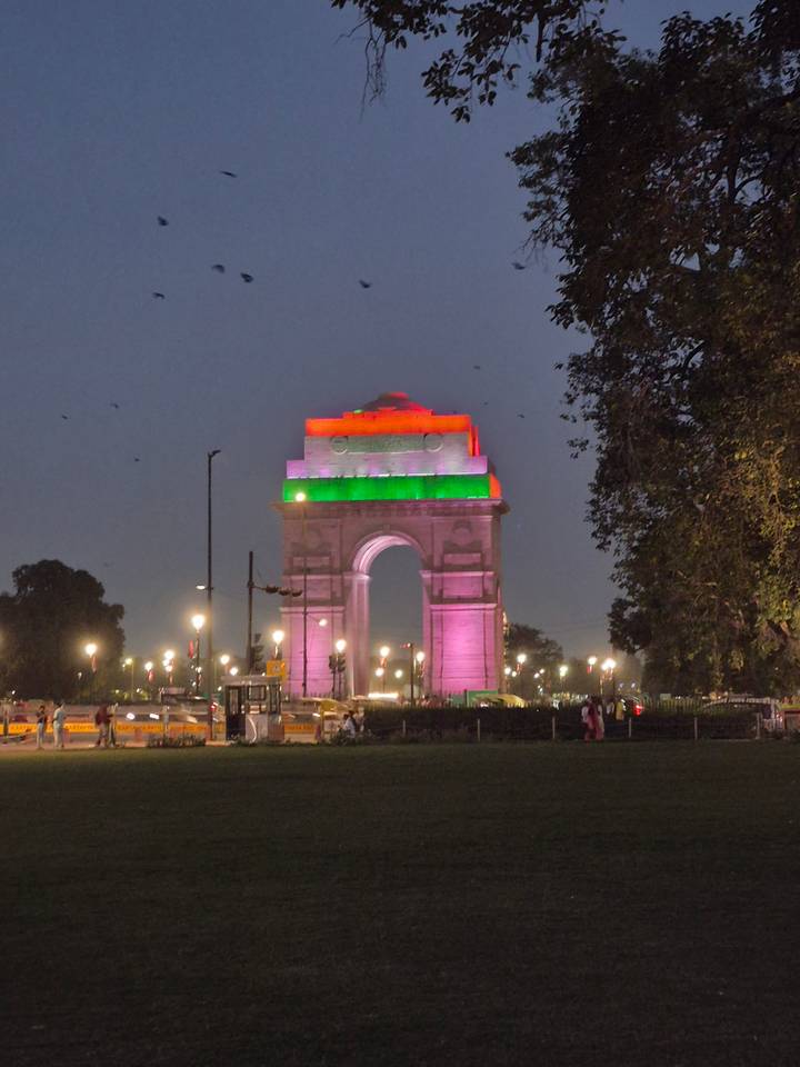 India Gate monument illuminated in tri-colour lights against the evening sky with traffic below.