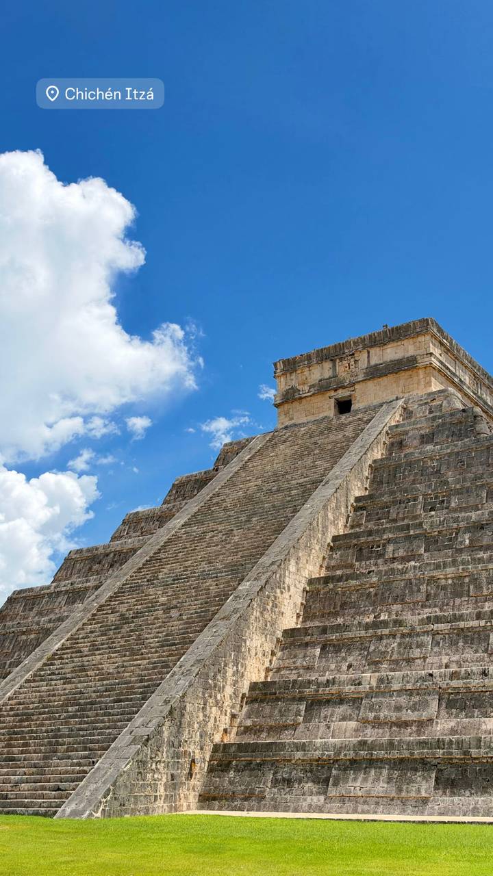 Stone pyramid temple rises steeply toward a blue sky with scattered clouds.