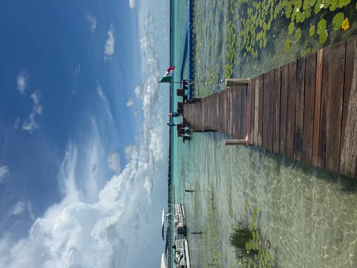 Wooden jetty stretches over crystal-clear turquoise lagoon toward open water and sky.