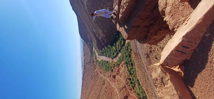 Traveller points across a green river valley carved between red cliffs.