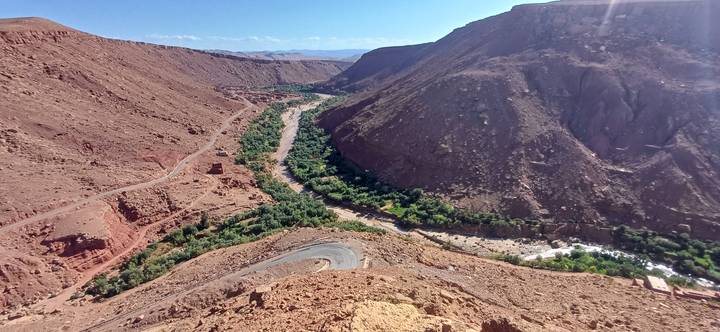 Wide view of winding river oasis and desert roadway amid rugged canyon terrain.