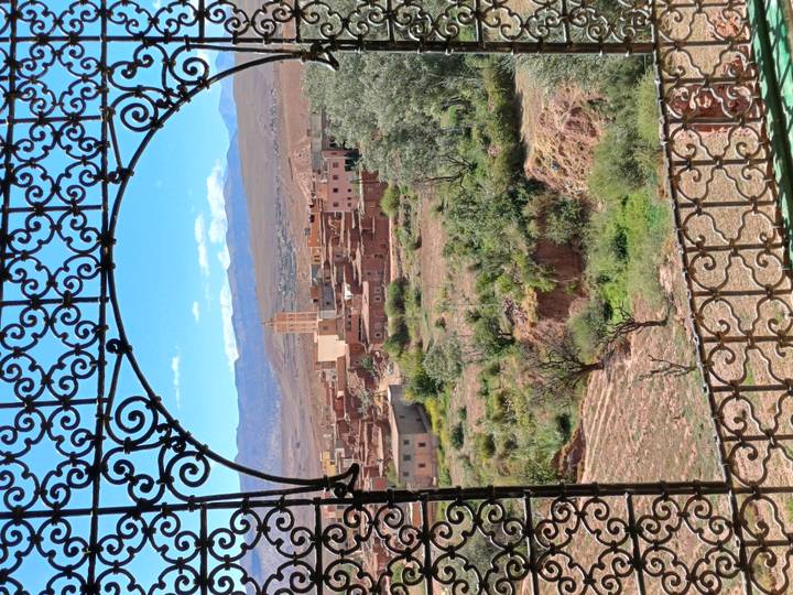 Rustic village and mosque tower framed by ornate wrought-iron window overlooking green valley.