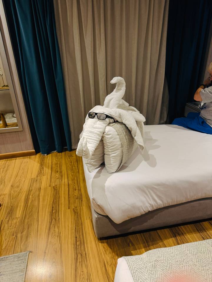 Playful towel sculpture wearing sunglasses placed on a neatly made cruise cabin bed.