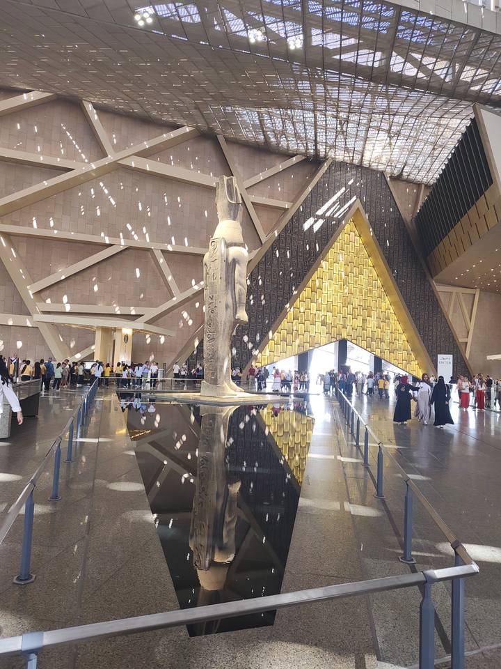 Grand Egyptian Museum interior with towering statue and crowds reflected in a polished black pool.