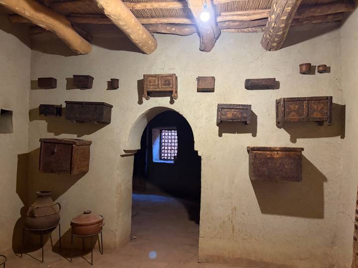 Traditional adobe interior with wooden chests and pottery displayed on rough plaster walls.