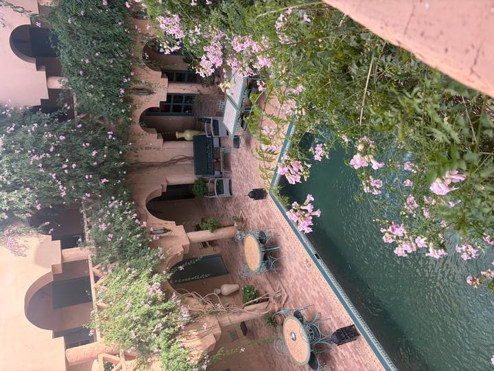Flower-covered riad courtyard with a small pool, arched balconies and cozy seating.