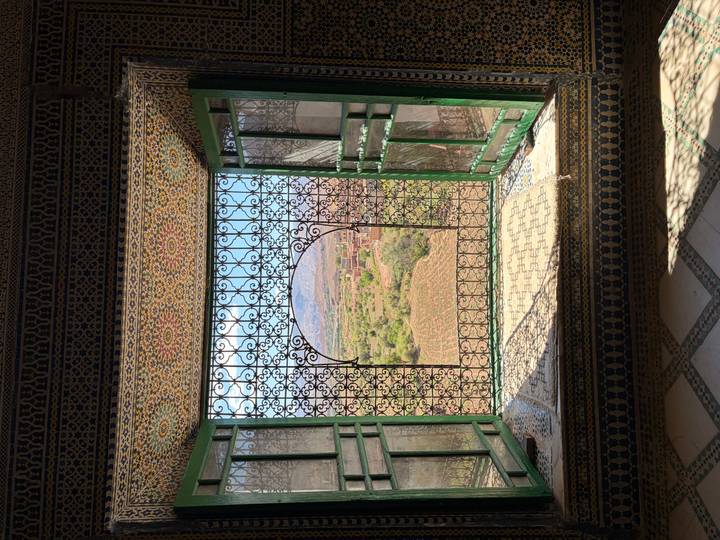 Ornate tiled window frame with wrought-iron grill opening to a panoramic valley and mountain view.