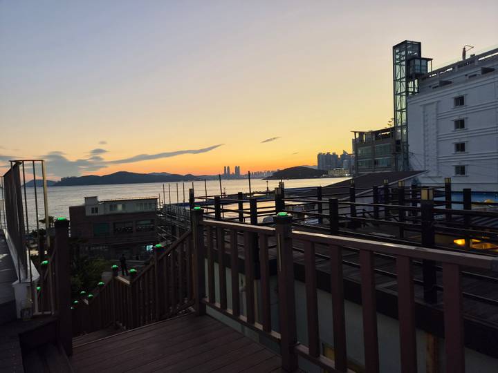 Soft sunset view over the bay with city skyline, small buildings and wooden railings in the foreground.