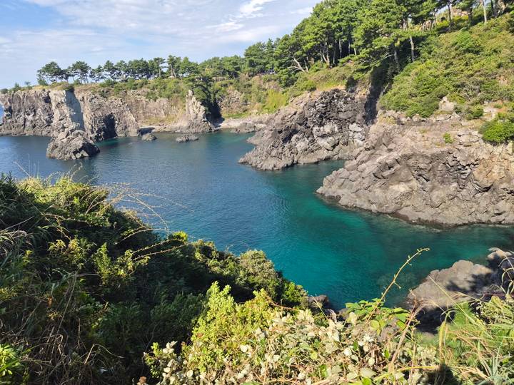 Clear turquoise bay surrounded by dramatic volcanic cliffs and lush greenery.