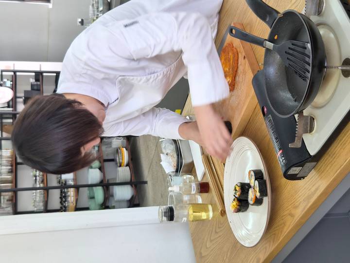 Chef in white prepares kimbap rolls during a hands-on cooking class.