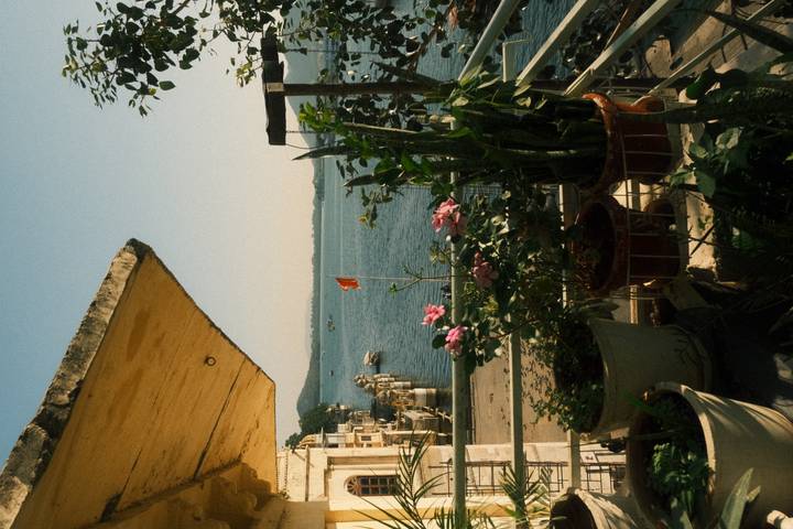 Balcony with potted plants overlooks a calm lake dotted with boats under clear blue sky.