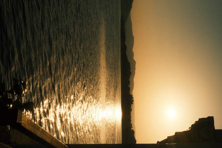 Golden sun sets over rippling lake waters with distant hills silhouetted.