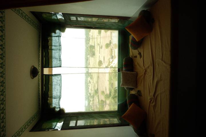 Cozy window alcove with cushions overlooks wide open desert plains through large glass pane.