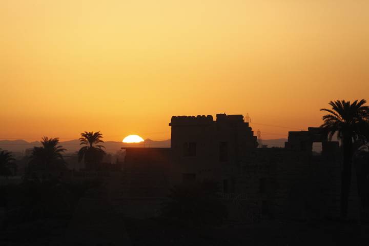 Orange sunset silhouettes palm trees and ancient ruins along the Nile.