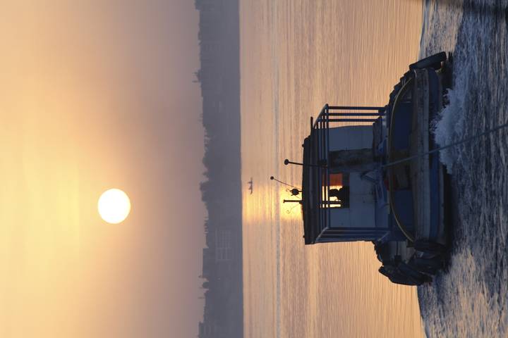 Small tugboat heads up the calm Nile at sunrise with golden orb over skyline.