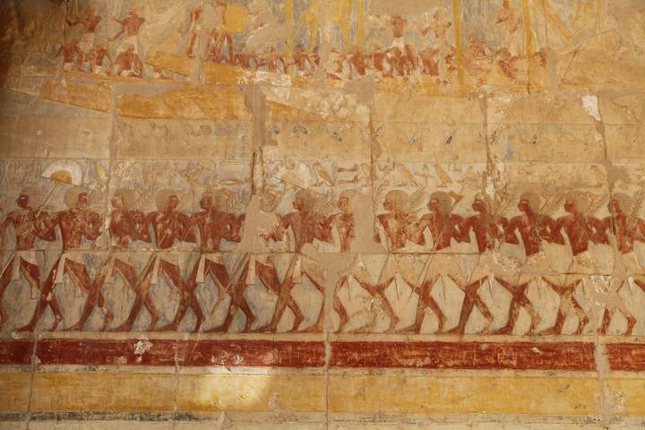 Ancient Egyptian wall relief of procession figures with faded pigments.