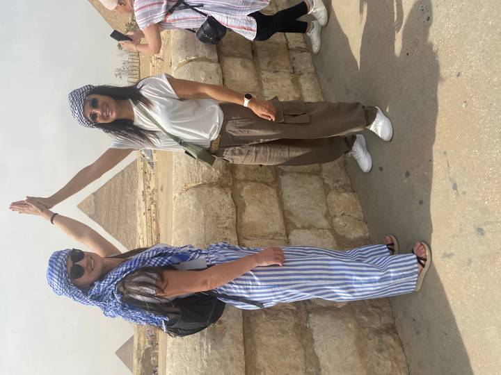 Two women high-five creating pyramid peak illusion with Great Pyramid of Giza behind.