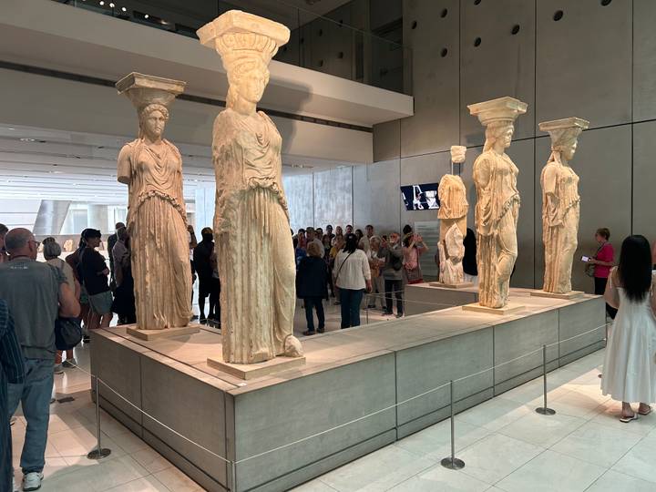 Visitors observe the original Caryatid statues displayed inside the Acropolis Museum.