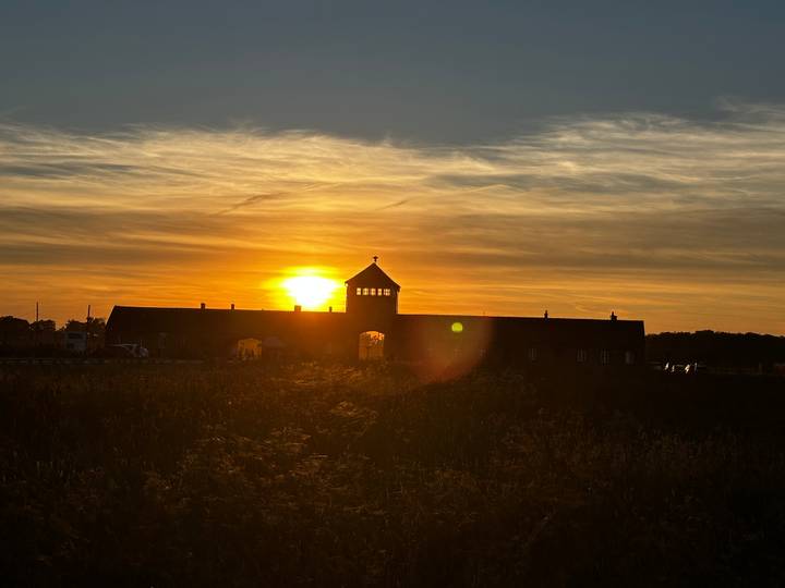 Silhouette of the Auschwitz Birkenau gatehouse against a dramatic orange sunset sky.