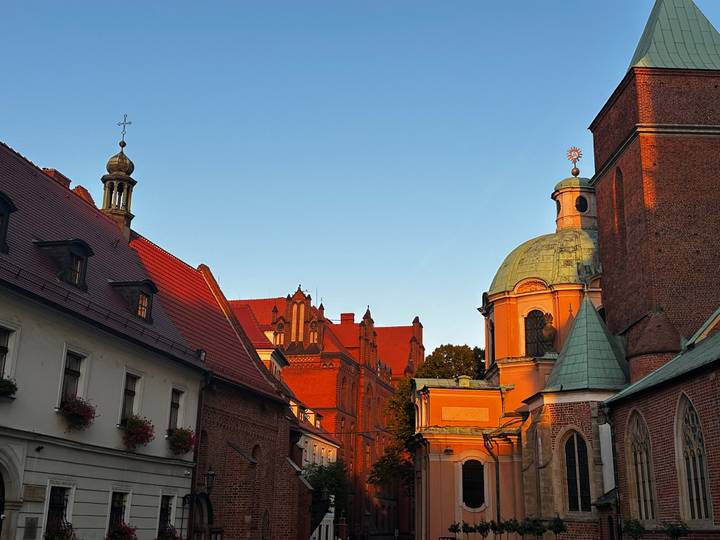 Warm evening light bathes red-brick historic buildings and church domes in a Polish old town street.
