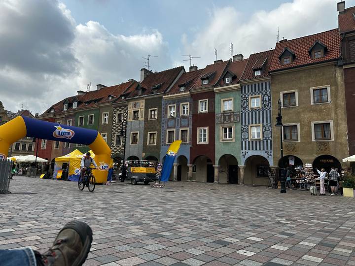 Colorful medieval merchant houses line Poznan’s Old Market Square with a cyclist passing an inflatable arch.