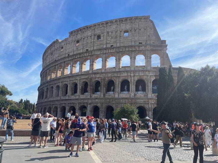 Rome’s Colosseum looms grandly as crowds of tourists explore the ancient amphitheater on a sunny day.