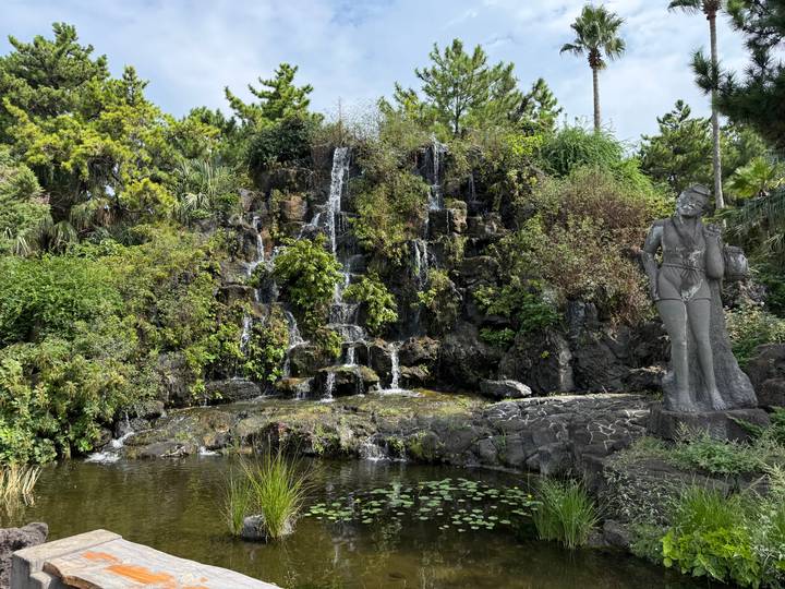 Rocky garden waterfall cascading into a pond surrounded by lush greenery and a statue