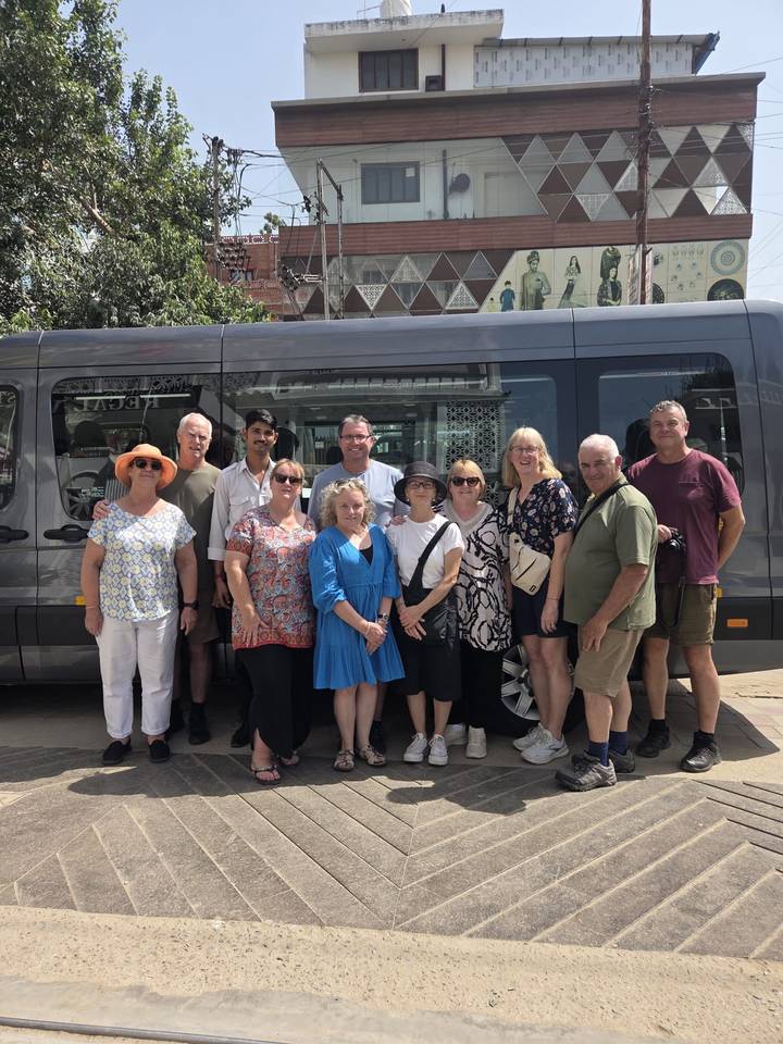 Tour group poses in front of their grey passenger van before departure.