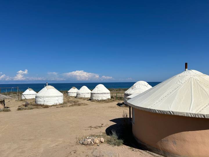 Row of white yurts lines the shore of a brilliant blue alpine lake under clear skies.