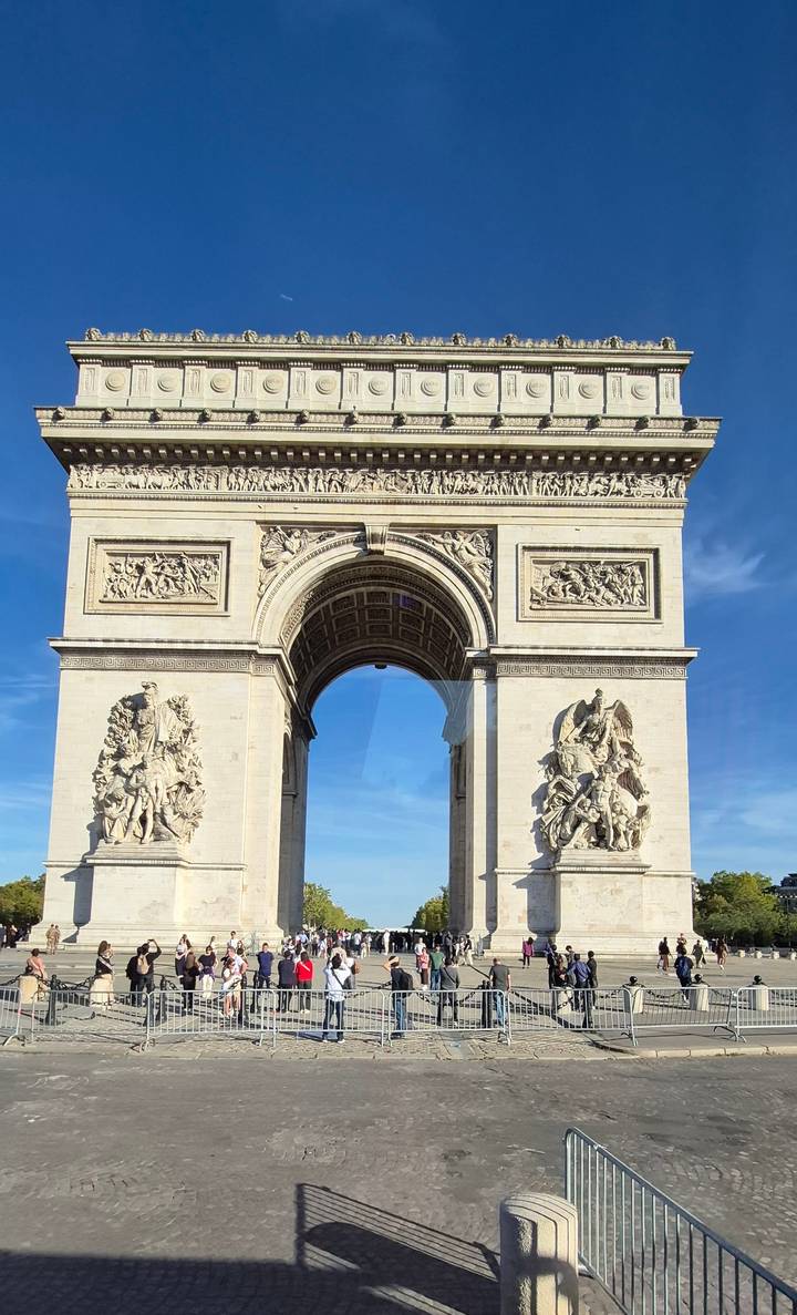 The Arc de Triomphe’s ornate carvings and arch rise majestically against blue sky.