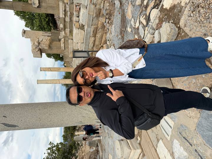 Playful couple strike poses amid fallen columns at an ancient archaeological site.