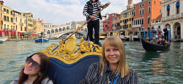 Women enjoy a gondola ride on Venice’s Grand Canal with the Rialto Bridge behind.