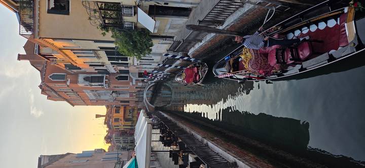 Serene Venetian canal at sunset with gondolier navigating beneath soft golden light.