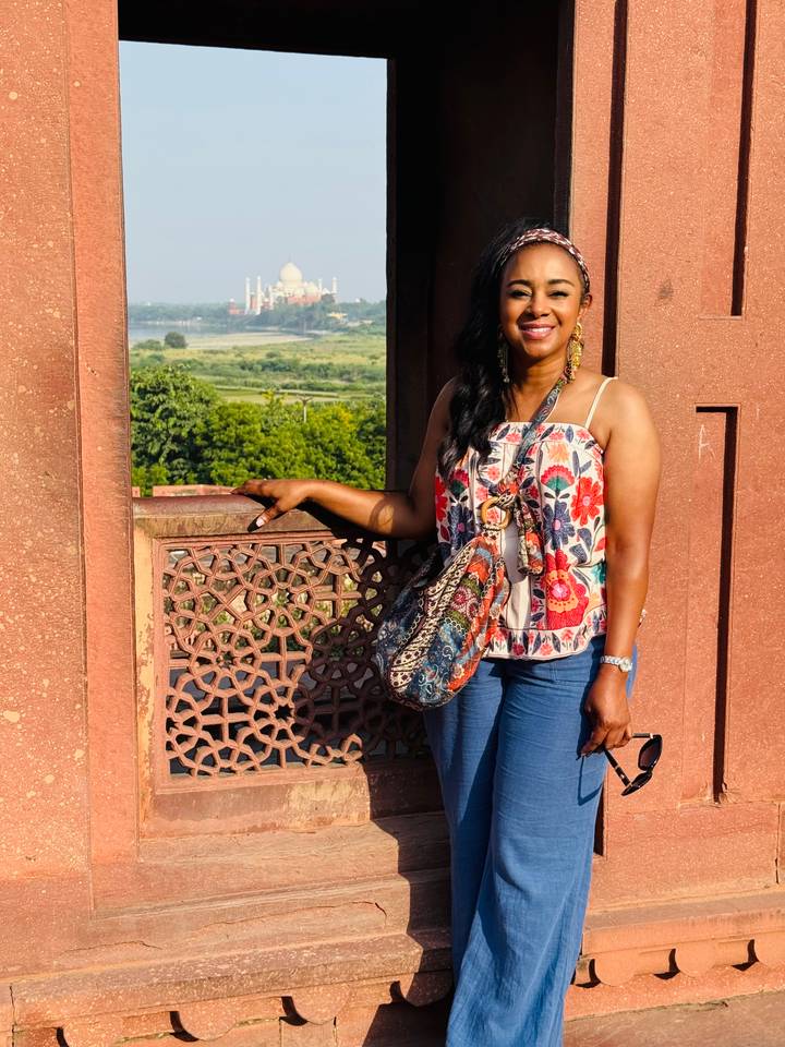 Tourist posing beside ornate red sandstone latticework with lush countryside visible through the opening.